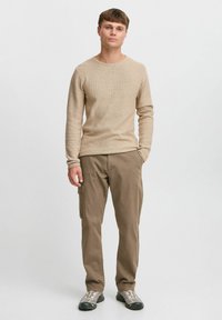 Beige ribbed long-sleeve shirt paired with loose-fitting brown cargo pants. Footwear is gray with a textured pattern. Simple, casual outfit.