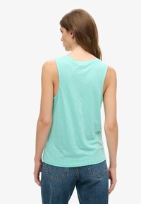 Top senza maniche verde menta realizzato in tessuto morbido, con scollatura rotonda e vestibilità rilassata, abbinato a jeans blu a vita alta.