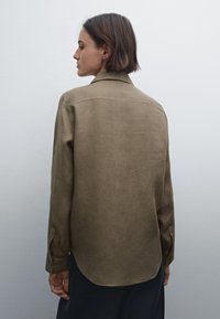 Olivgrön linne skjorta med krage, rundad nederkant och knäppta ärmar, som visar en mjuk textur och en avslappnad passform.
