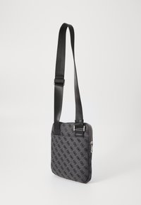 Bolso cruzado negro con estampado que cuenta con un cierre de cremallera, una correa ajustable y una textura suave. Forma cuadrada compacta con detalle del logo.