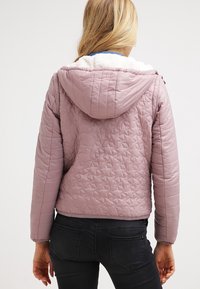 Světle růžová prošívaná bunda s kapucí, s měkkou bílou vnitřní podšívkou. Navržena v přiléhavém střihu s texturovaným vzorem na látce.