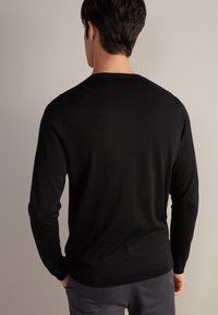 Maglietta nera a maniche lunghe realizzata in un tessuto morbido, con scollatura rotonda e vestibilità rilassata, caratterizzata da cuciture minime e una superficie liscia.