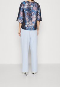 Bluse mit floralem Muster in Dunkelblau und Lila mit glänzenden Akzenten, kombiniert mit hellblauen weit geschnittenen Hosen und silbernen High Heels.