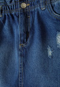 Tissu en denim bleu avec une finition texturée. Comprend une taille élastique, une poche avant et des patchs déchirés avec des bords effilochés.