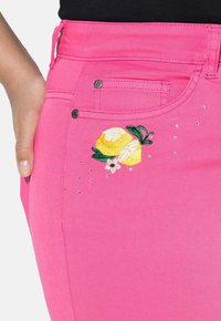 Vaaleanpunaiset farkut, joissa on brodattu sitruunakuvaus kukka-aiheilla ja pienillä strasseilla koristeltuina taskuissa.