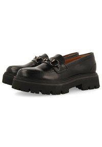 Mocassins en cuir noir avec une semelle en caoutchouc épaisse, ornés de quincaillerie métallique sur le dessus et d'une silhouette épurée. Adhérence texturée sur la semelle extérieure.