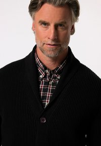 Černý žebrovaný svetr s šálovým límcem, se single fialovým knoflíkem. Nosit přes černou a červenou kostkovanou košili s bílými akcenty.