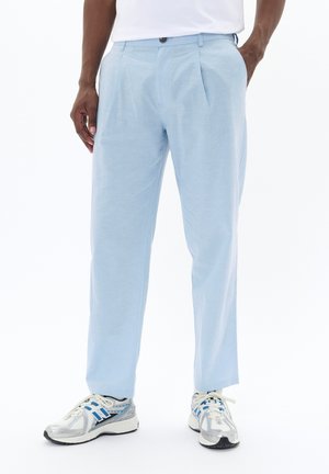 Light blue trousers with front pleats and belt loops. Made from textured fabric. Paired with silver and blue athletic shoes.