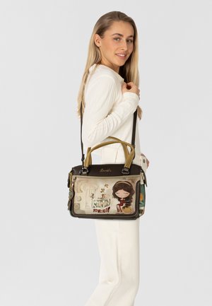 Schwarze und beige Handtasche mit einer dekorativen Illustration eines Mädchens und Text. Mit zwei Griffen, einem Schultergurt und einzigartigen Verzierungen.