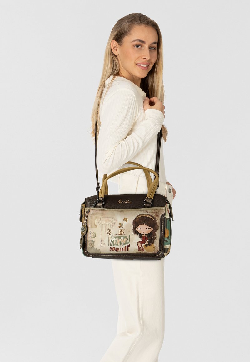 Schwarze und beige Handtasche mit einer dekorativen Illustration eines Mädchens und Text. Mit zwei Griffen, einem Schultergurt und einzigartigen Verzierungen.