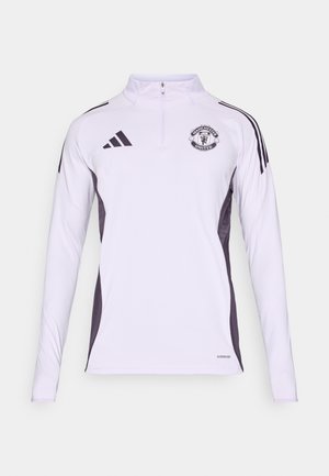 Camiseta deportiva blanca de manga larga con cremallera de un cuarto, paneles laterales negros y logo de Manchester United en el pecho. Hecha de material suave y ligero.