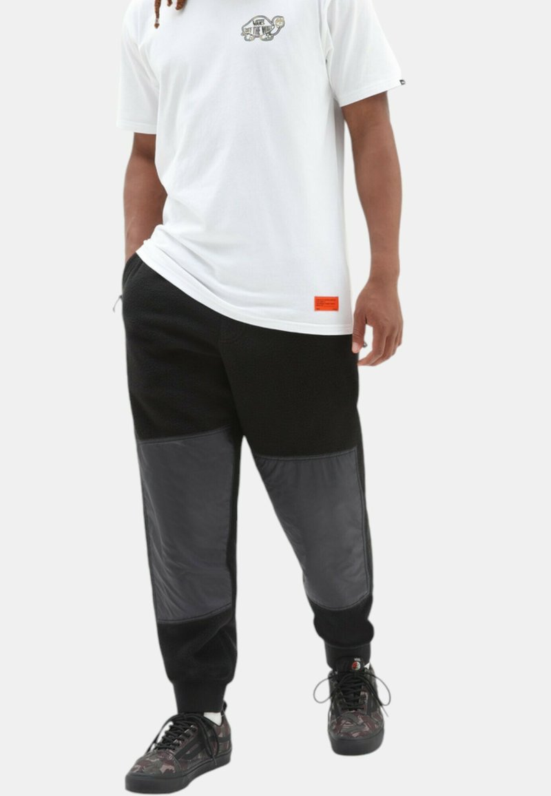 Hvid T-shirt med grafiktryk, parret med sorte bukser med grå paneler og ribbede manchetter. Sorte sneakers fuldender looket.