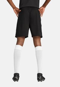Schwarze Sportshorts mit elastischem Taillenbund, kombiniert mit weißen knielangen Socken und schwarzen Fußballschuhen mit strukturiertem Design.