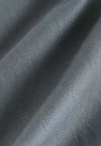 Harmaa kangas, jossa on sileä pinta, näyttäen hienovaraisia poimuja ja hienoa kudontakuvioita. Materiaali vaikuttaa kevyeltä ja hengittävältä.