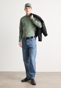Cămașă verde cu nasturi, blugi albaștri, curea neagră și cizme negre. Geacă neagră aruncată peste umăr. Textură moale, stil casual.
