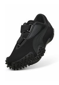 Chaussure de sport noire avec crampons texturés sur la semelle, tissu en maille et deux sangles velcro réglables avec boucles métalliques.