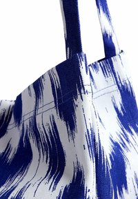 Blue and white patterned tote bag made of textured fabric, featuring long straps and a structured shape. Pattern resembles brush strokes.