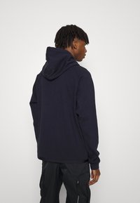 Marineblaue Kapuzenjacke aus weichem Stoff, mit Kordelzugkapuze, langen Ärmeln und entspannter Passform. Die Rückansicht zeigt die Nahtdetails.