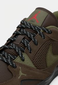 Baskets marron et vert olive avec des lacets noirs, avec un logo Jumpman rouge sur la languette et des côtés en mesh texturé.
