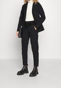Giacca trapuntata nera abbinata a pantaloni neri aderenti. L'outfit presenta un dolcevita bianco e nero e stivali neri chunky. Inclusa una borsa semplice.