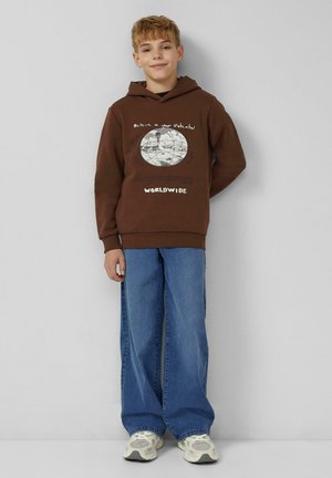 Brauner Kapuzenpullover mit einer Globusgrafik und Text, kombiniert mit weit geschnittenen blauen Jeans und beigen Turnschuhen. Glatte Textur, lässige Passform.