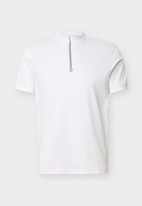 Λευκό πόλο μπλουζάκι με κοντά μανίκια, ψηλό γιακά και φερμουάρ μπροστά, απλό σχέδιο, τοποθετημένο σε επίπεδο φωτεινό φόντο.