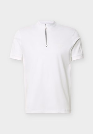 Λευκό πόλο μπλουζάκι με κοντά μανίκια, ψηλό γιακά και φερμουάρ μπροστά, απλό σχέδιο, τοποθετημένο σε επίπεδο φωτεινό φόντο.