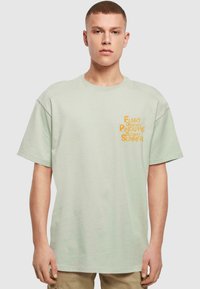 Lysegrøn bomulds t-shirt med korte ærmer. Har fedt orange tekst: "Funky Dancing Pineapple Sizzling Summer." Casual pasform.