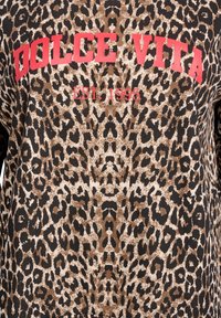 Tkanina so vzorom leoparda s výrazným červeným textom „DOLCE VITA“ a menším červeným textom „EST. 1995“ umiestneným v strede vpredu.