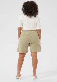 Kaki shorts med elastisk midjeband, mittlånga, och avslappnad passform, ihop med en åtsittande vit topp och ljusa klackar.