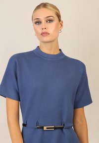 Abito azzurro a maniche corte con scollatura alta, tessuto testurizzato e una cintura nera con un accento rettangolare dorato.