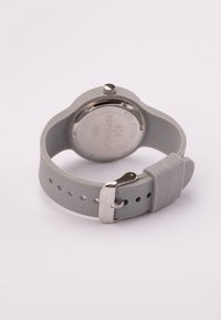 Reloj de silicona gris con textura suave, caja redonda, corona de metal y fondo de acero inoxidable, que cuenta con una hebilla plateada y agujeros para ajustes.