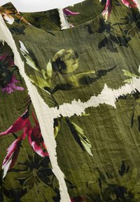 Sukienka w kwiatowy wzór z oliwkowo-zielonym tłem oraz różowymi i białymi akcentami. Wykonana z lekkiego materiału o teksturowanej powierzchni.