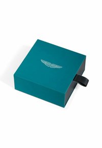 Scatola di cartone color teal con finitura opaca, con logo Aston Martin bianco e una linguetta di tessuto nero su un lato.