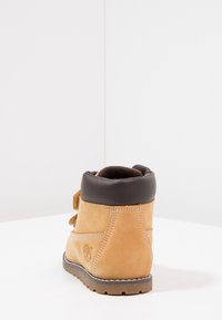 Botín de cuero marrón con acentos de ante beige, cuello acolchado y suela texturizada. Diseño con cordones y logotipo visible en el lado.