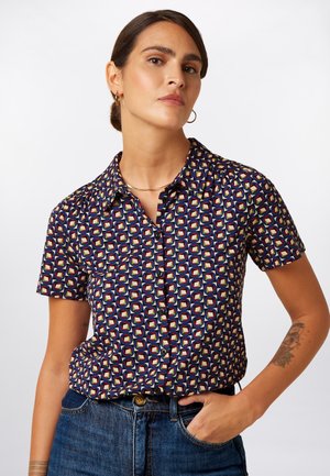 Kortærmet skjorte i mørkeblå stof med et geometrisk mønster i rød, grøn og gul. Har en klassisk krave og knaplukning.