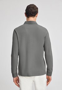 Långärmad polo skjorta i grått, med mjuk textur, krage och manschetter. Baksidan visar en enkel och ren design utan mönster.