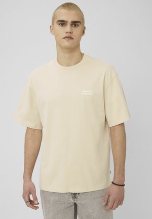 T-shirt en coton beige à manches courtes et col rond. « Idea in progress » imprimé en petits caractères blancs sur la poitrine. Coupe décontractée.