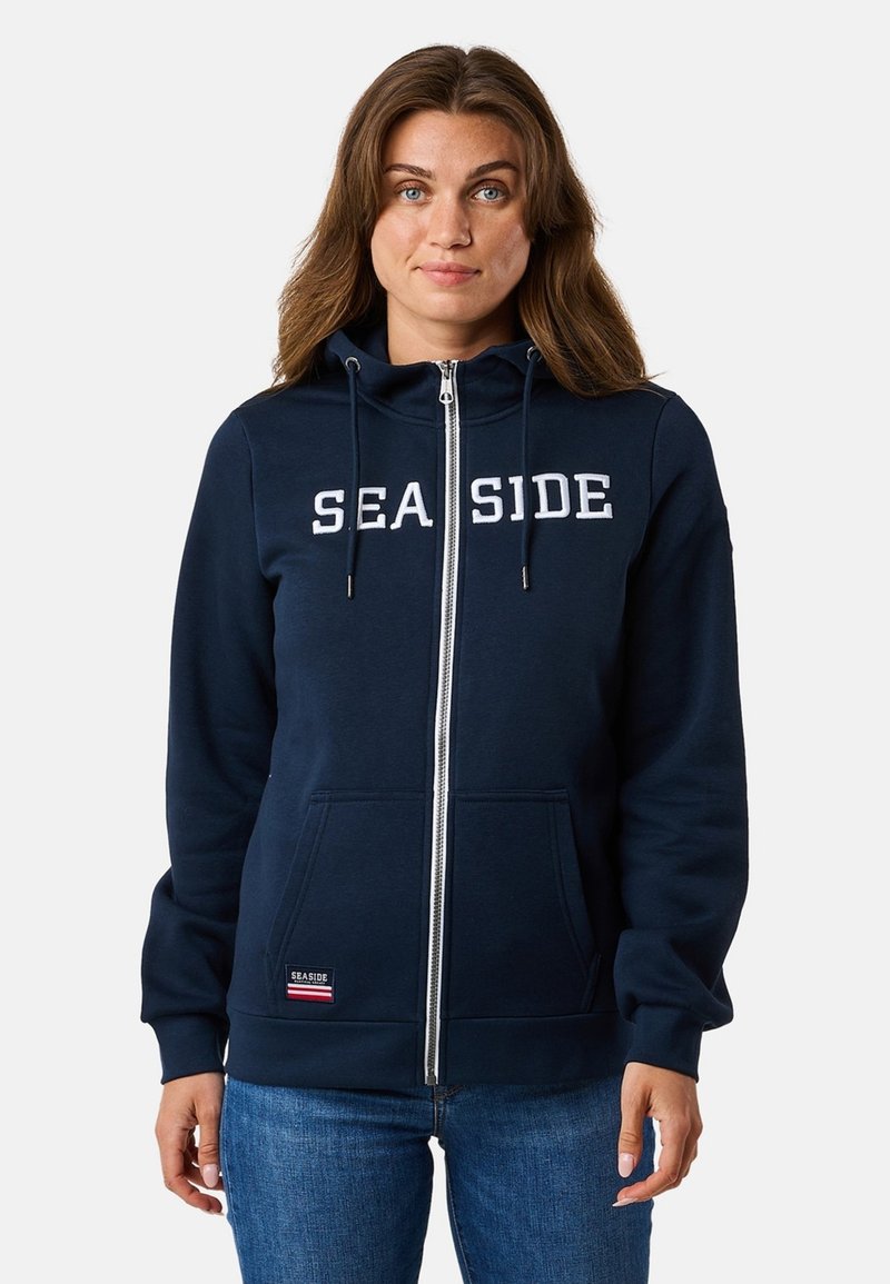 Marine zip-up hoodie gemaakt van zachte stof, met een grote "SEASIDE" bedrukking in het wit, een trekkoordkap en voorzakken met een logo-applicatie.
