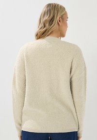 Pullover color crema, strutturato, con scollo rotondo e spalle scese. Polsini e orlo a costine, realizzato in materiale morbido e soffice.