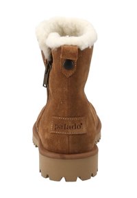 Stivaletti alla caviglia in suede marrone con una fodera bianca pelosa, cerniera laterale, linguetta posteriore con un bottone nero e suola in gomma con texture.