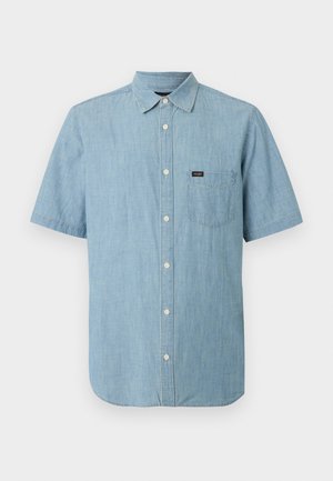 Ανοιχτό μπλε πουκάμισο με κοντά μανίκια, κουμπιά, γιακά και μία τσέπη στο στήθος που φέρει μια μικρή μαύρη ετικέτα της μάρκας.