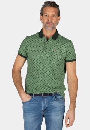 Groene polo met patroon en een donkere groene kraag, korte mouwen en sluiting met drie knopen. Draagt het met lichtblauwe jeans en een zwarte riem.