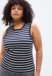 Μπλε σκούρο και λευκό ριγέ τοπ χωρίς μανίκια, κατασκευασμένο από απαλό, λείο ύφασμα. Διαθέτει στρογγυλή λαιμόκοψη και λεπτομέρεια με λογότυπο στο στήθος.