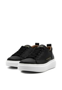 Sneakers neri in pelle con suole bianche spesse, dotati di lacci neri e un logo dorato sul lato. Texture liscia e design aerodinamico.