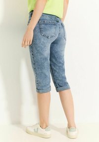 Helle blaue Denim-Capri-Jeans mit umgeschlagenen Säumen, ausgestattet mit aufgesetzten Taschen und subtilen Ausbleichungen, kombiniert mit weißen Sneakern.