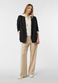 Czarna dwurzędowa marynarka na kremowej bluzie z kapturem, zestawiona z jasnobeżowymi szerokimi spodniami i białymi tenisówkami, prezentująca swobodny, warstwowy styl.