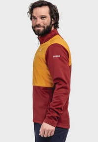 Zweifarbige Fleecejacke in Rot und Gelb, mit hohem Kragen und langen Ärmeln. Logo auf der linken Schulter.