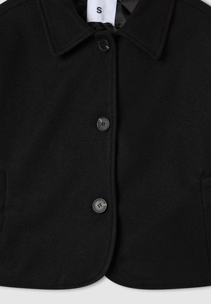Giacca nera in misto lana con colletto, quattro bottoni e due tasche laterali. Forma corta e squadrata, texture liscia, etichetta delle taglie visibile.