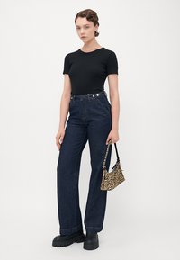 Woman wearing black fitted short-sleeve top, high-waisted dark jeans, black chunky shoes, holding small zebra-print handbag.